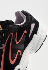 Svarta sneakers med rosa och orange detaljer, tillverkade av en blandning av mocka och nätmaterial, med en texturerad sula och en vadderad ankelflik.