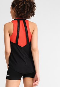 Schwarzes und rotes Sporttanktop mit Racerback-Design, schwarzen Trägern, kontrastierenden Farben und glatter Textur. Eignet sich hervorragend für Sportbekleidung.
