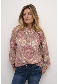 Blouse à manches longues en tissu léger et à motifs, présentant des motifs floraux en rose, orange et bleu, avec un col froncé et des poignets élastiques.