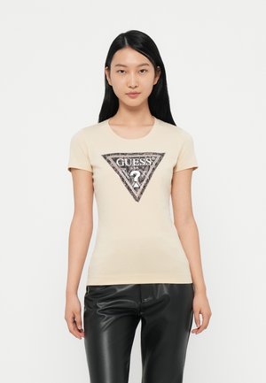 Lichtbeige t-shirt met korte mouwen, met een zwart en zilver driehoekig logo met de tekst "GUESS?" en decoratieve accenten in het midden.