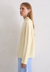 Jasnożółty sweter z golfem, z długimi rękawami, luźny krój i miękka tekstura. Nosi się go na jasnoniebieskich spodniach z kordury, o minimalistycznym designie.