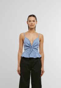 Lys blå peplum topp med ribbet tekstur, dyp V-hals, justerbare stropper og en knytedetalj foran. Kombinert med svarte vide bukser.