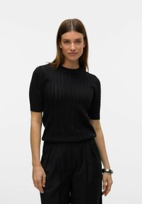 Černý pletený top s krátkým rukávem, který má texturovaný vzor s vertikálními pruhy. Doplněn černými kalhotami s vysokým pasem a hodinkami.