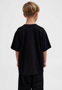 Schwarzes Baumwoll-T-Shirt mit kurzen Ärmeln und rundem Ausschnitt, von hinten betrachtet. Kombiniert mit schwarzen Hosen, ohne sichtbare Muster oder Akzente.
