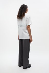 Fehér, rövid ujjú pamutpóló, hátul kék felirattal. Szürke csíkos, széles szárú nadrággal és fekete cipővel párosítva.