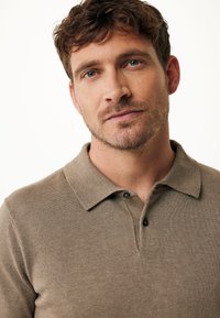 Brun stickad polo med krage, med en tre-knapps knappslå och subtil textur. Neutral färg och avslappnad design.