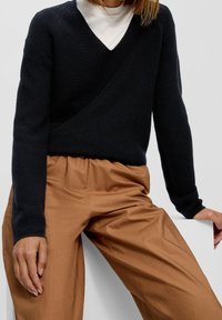 Marineblauwe gebreide trui met een diepe V-hals, gecombineerd met beige wijde broekspijpen. De trui heeft een geribbelde textuur en lange mouwen.