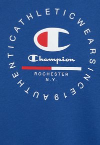Modrá bavlněná mikina s kulatým grafickým prvkem s nápisem "Champion" v písmu, logem s červenými a bílými akcenty, a textem "ROCHESTER N.Y." pod ním.