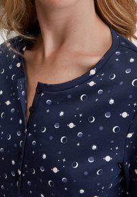 Top blu navy con scollatura rotonda, bottoni e un motivo celestiale che presenta lune e pianeti in toni di bianco e azzurro chiaro.