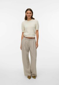 Pull en maille crème à manches courtes, associé à un pantalon taille haute gris clair. Une ceinture marron souligne la taille. Des chaussures vert olive complètent le look.