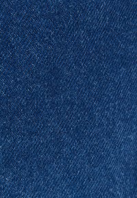 Tela de mezclilla azul con una textura suave, que presenta un tejido de sarga clásico. Las puntadas están distribuidas de manera uniforme, mostrando ligeras variaciones de color.