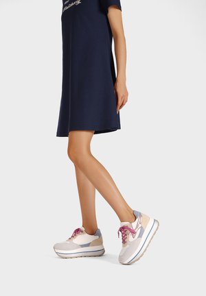 Sneakers leggeri che presentano una combinazione di materiali bianchi, grigi e rosa, con pannelli testurizzati e lacci viola, abbinati a un vestito blu navy.