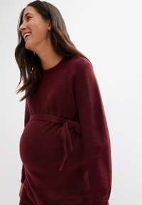 Burgunder Schwangerschafts-Pullover aus weichem Stoff, mit langen Ärmeln, einem runden Halsausschnitt und einem Taillenzug für eine verstellbare Passform.