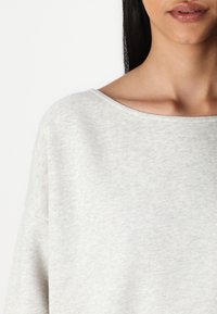 Haut à manches longues texturé gris clair avec un large col et une coupe relaxée. Tissu doux avec un motif subtil pour le confort et la polyvalence.