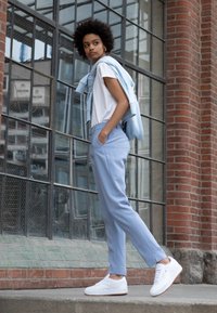 Svetlo modri hlače krojenega kroja, v kombinaciji z belim majico in svetlo modrim puloverjem, ki je položen čez ramena; bele superge zaokrožajo outfit.