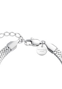 Pulsera de cadena de plata con un diseño de eslabones texturizados, que incluye un broche de langosta y una etiqueta circular de marca. Acabado suave en toda la superficie.