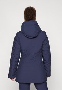 Marineblå puffjakke med hette, med en jevn tekstur, figursydd design og sømde detaljer langs sidene og ermene.