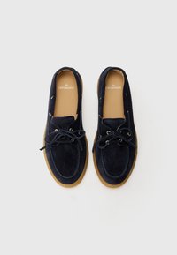 Marineblaue Wildlederschuhe mit gebundenen Schnürsenkeln, Gummisohle und sandfarbenen Akzenten. Mit einer gesteppten Detailverarbeitung im Obermaterial und einem Logo auf der Innensohle.