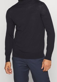 Marinefarbener Rollkragenpullover aus weichem Strickmaterial. Besitzt enganliegende lange Ärmel sowie gerippte Bündchen und Saum für einen schlanken Look.