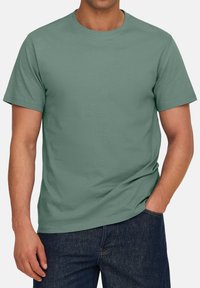 T-shirt verde in cotone con scollo rotondo e maniche corte, caratterizzato da una vestibilità comoda. Abbinato a jeans scuri, senza motivi né grafiche.