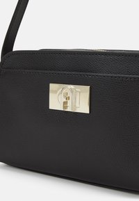 Borsa a tracolla nera in pelle con texture, dotata di una chiusura in metallo dorato e dettagli cuciti, caratterizzata da una tracolla sottile e forma rettangolare.