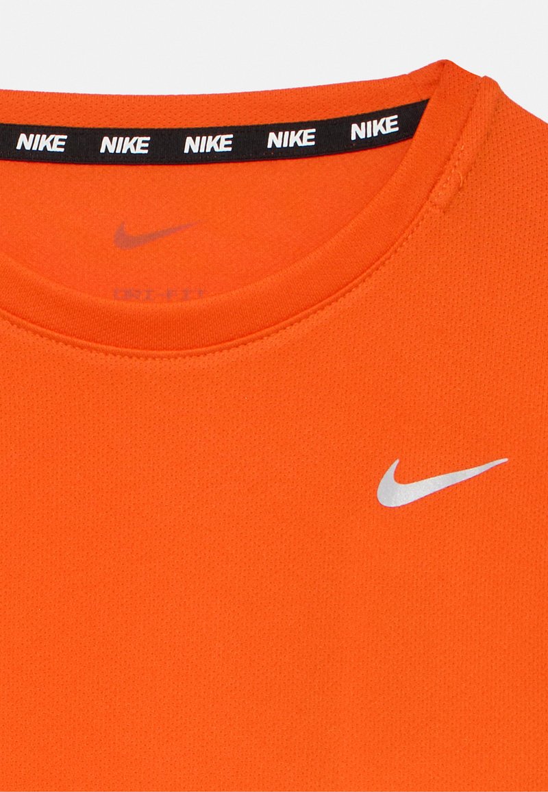 T-shirt Nike orange avec un col rond, comportant une bande de col noire arborant le nom de la marque répété et un petit logo argenté sur la poitrine.