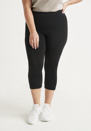 Czarne legginsy capri wykonane z elastycznego materiału, z wysokim pasem, w połączeniu z białymi butami sportowymi i neutralną górą.