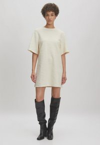 Crème-kleurige jurk met korte mouwen van een textuur stof, tot op de knie. Gecombineerd met zwarte kniehoog laarzen en eenvoudige sieraden accenten.