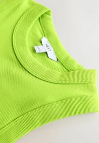 Grünes, geripptes Tanktop mit weitem Rundhalsausschnitt und einem Etikett mit der Aufschrift "NEXT". Glatte Textur, figurbetontes Design und lebendige Farbe.