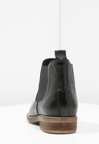 Stivale alla caviglia nero in pelle con finitura texture, lati elasticizzati e tacco impilato. Destinato a colpire per il suo design elegante e minimalista.