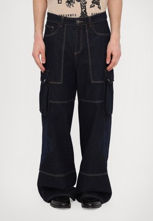 Dark blue cargo pants with side pockets, wide leg design, contrasting orange stitching, and a smooth denim texture.