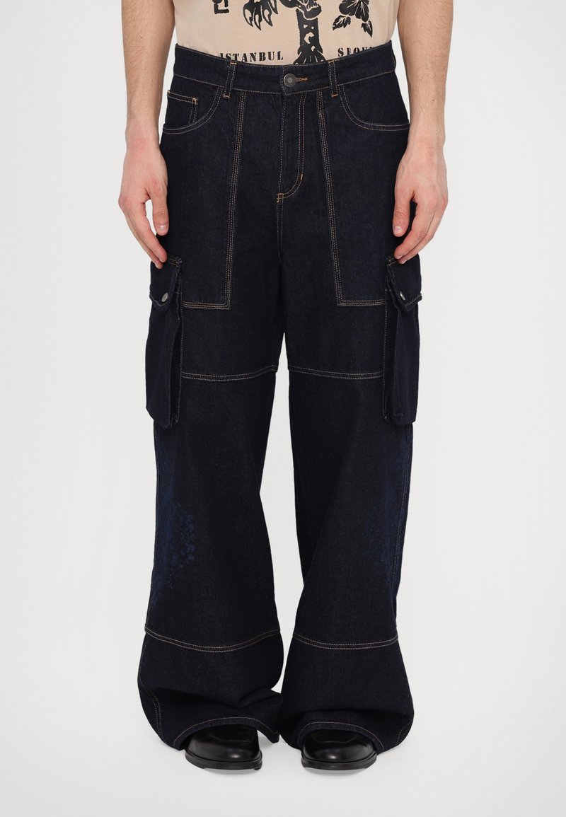 Pantalons cargo bleu marine avec poches latérales, design à jambes larges, surpiqûres orange contrastantes et texture denim lisse.
