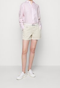 Ljust rosa och vit randig långärmad skjorta, beige shorts, vita sneakers med guld accenter, och ett vitt bälte med en silver spänne.