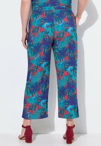 Pantaloni a gamba larga con stampa floreale in una combinazione di colori turchese, rosso e verde; tessuto leggero; orlo sopra la caviglia, abbinati a sandali con tacco rossi.