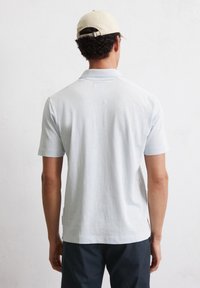 Lichtgrijze polo met korte mouwen, relaxte pasvorm, zachte stof, platte gebreide kraag en een rechte zoom, gecombineerd met donkere broeken en een beige pet.