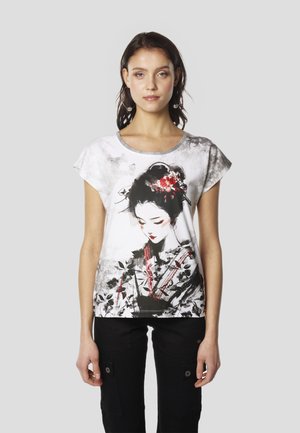 Fehér rövid ujjú póló, amely egy hagyományos öltözetet viselő nőt ábrázoló grafikával díszített, virágos elemekkel és piros részletekkel.