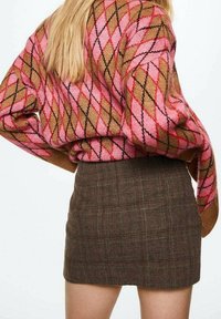 Pull en maille avec motif argyle en rose, marron et noir, associé à une mini-jupe ajustée à carreaux marron. Texture douce, design décontracté.