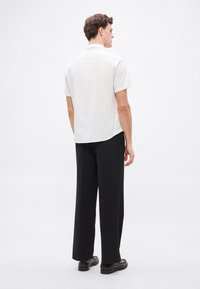 Trumpomis rankovėmis balti polo marškinėliai su lygia tekstūra, derinami su juodomis plačiomis kelnėmis ir juodais batais; matomi iš nugaros.