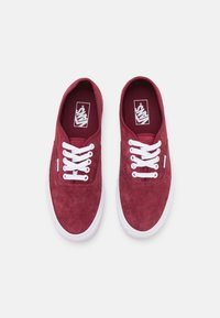 Røde semskede sneakers med hvide snørebånd, der har et lavt design og en struktureret overdel, mærket indersål og hvid gummisål.