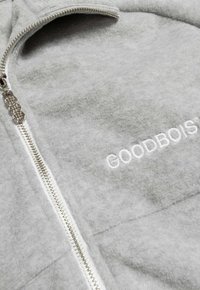Grau zip-up Jacke aus weichem Material; verfügt über einen metallischen Reißverschluss und gestickten "GOODBOIS"-Text in Weiß.