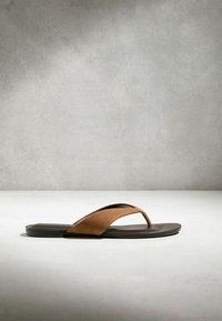 Sandale en suède marron avec semelle plate noire sur une surface et un arrière-plan gris texturé.