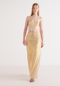 Goldfarbene Satin-Halterkleid mit tiefem V-Ausschnitt, seitlichen Ausschnitten und einem floralen Akzent in der Taille. Glatte Textur und bodenlanger Schnitt.