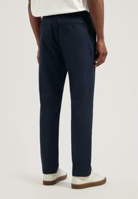 Marineblauwe broek met een rechte snit, gemaakt van zachte stof. Heeft een ontspannen tailleband en twee achterzakken met knoopsluitingen.
