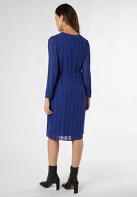 Blaues plissiertes Kleid mit langen Ärmeln, einem Rundhalsausschnitt und einer taillierten Taille; kombiniert mit schwarzen Knöchelstiefeln und einer glatten Textur.
