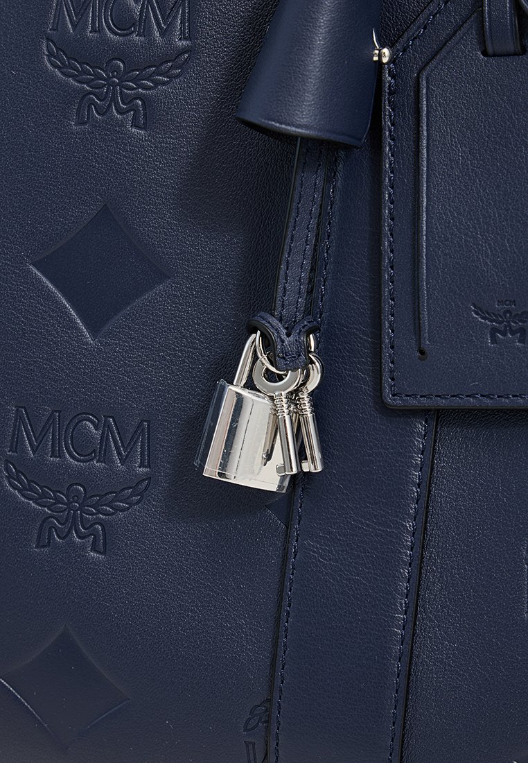 Marineblaue Lederhandtasche mit geprägtem MCM-Logo, Diamantmuster und silbernen Hardwareelementen. Sie verfügt über ein Schloss und Schlüssel, die seitlich angebracht sind.