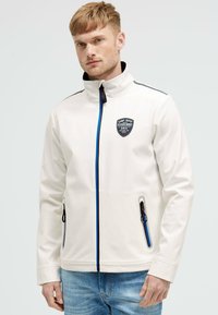 Giacca softshell bianca con colletto alto, zip blu e nere, tasche laterali e un patch con logo sul petto.