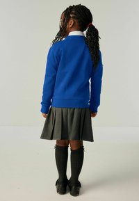 Plava dukserica s dugim rukavima, siva nabirana suknja, crne čarape do koljena s rebrastim uzorkom i crne cipele. Pogled straga.