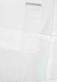 Witte stof met een gladde textuur, met contrasterende stiksel. Er is een zakflap aanwezig met een dunne horizontale streepdetail.