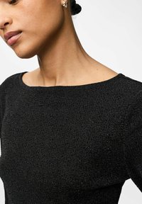 Schwarzes strukturiertes Kleid mit einem weiten, runden Ausschnitt, das ein dezentes Muster und Schimmer aufweist. Nahaufnahme, die die Schulter- und Halsdetails zeigt.