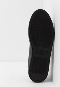 Semelle de sneaker en caoutchouc noir avec des motifs en vague, présentant une section rectangulaire étiquetée "A X". Bords lisses et détails minimaux.